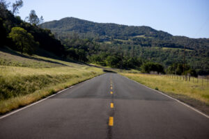 two-lane flat and straight road with fields on either side and mountain in the background